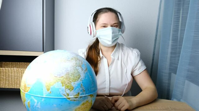 girl with long hair wearing headphones, medical mask leading conference, shows place on the globe from home office, concept of remote education, video conference, foreign language lesson