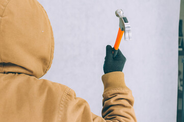 A man holds a construction hammer in his hands on a light background.