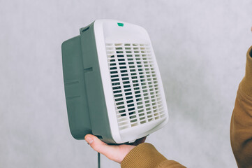 A man holds a heater in his hands on a light background.