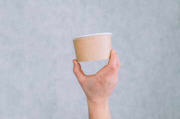 A man holds a mock-up of a paper cup for soup, coffee and tea on a light background.