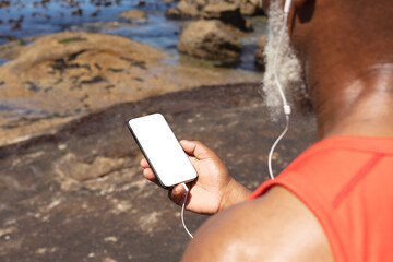 Senior african american man wearing earphones using smartphone by the sea