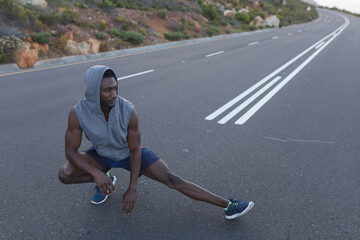 Fit african american man in sportswear stretching on a coastal road