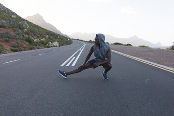 Fit african american man in sportswear stretching on a coastal road