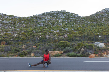 Fit african american man in sportswear stretching on a coastal road