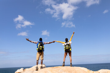 Fit afrcan american couple wearing backpacks hiking holding hands on the coast