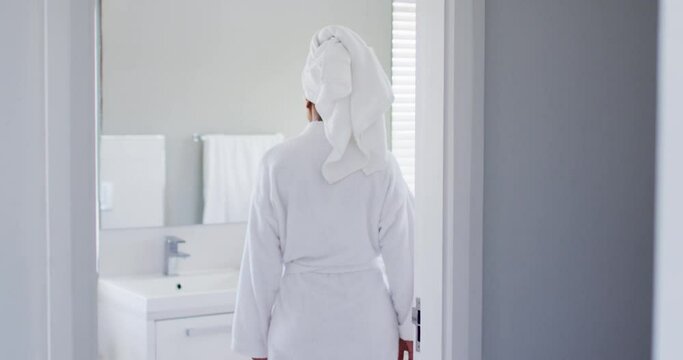 African american woman in bathrobe touching her face looking in the mirror at bathroom