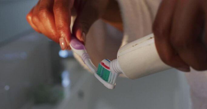 Close up of african american woman putting toothpaste on her brush in the bathroom