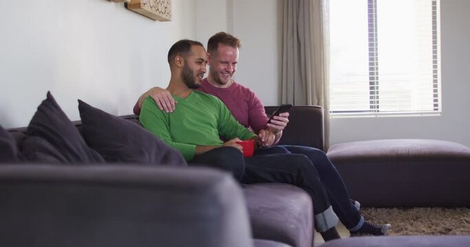 Multi ethnic gay male couple sitting on couch looking at smartphone together