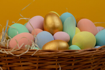 Fototapeta na wymiar Wicker basket with colorful Easter eggs in pastel colors on yellow background