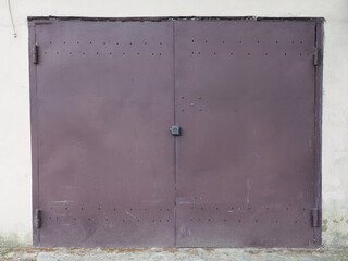 Closed iron brown garage door with holes at the top and bottom and splashing mud