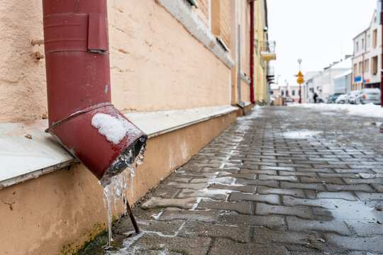 The drainpipes are covered with ice and snow. After a heavy snowstorm, the city is covered with snow and ice. There are many icicles on the facade of the building. Ice on sidewalks and roads.