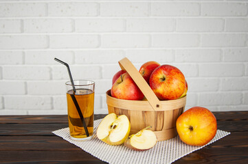 beautiful apples in a wooden basket on a wooden surface and a glass of apple juice