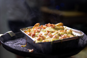 bandeja de patatas con queso fundido y jamón recién salida del horno