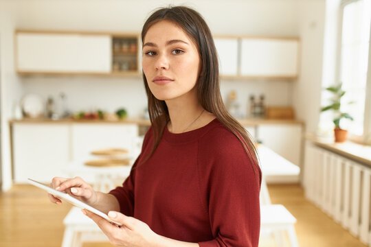 Attractive young woman freelancer in casual clothing surfing internet or playing video games using wireless high speed connection on digital tablet. Cute female posing indoors with portable computer