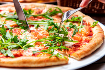 Appetizing pizza in a cafe. The visitor cuts the pizza with a knife and fork at the table.