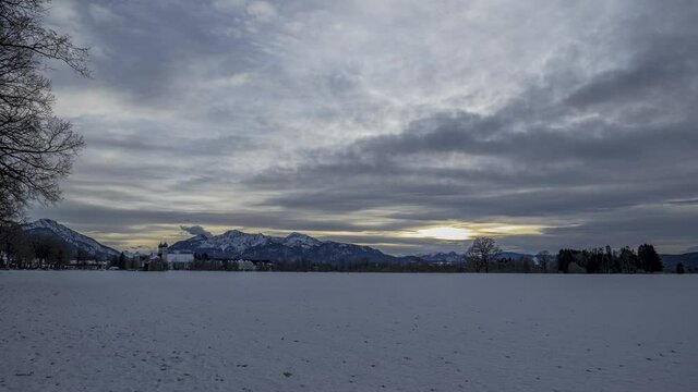 Zeitraffer Sonnenuntergang im Winter mit Voralpenlandschaft und Koster Benediktbeuren bei bew&ouml;lktem Himmel