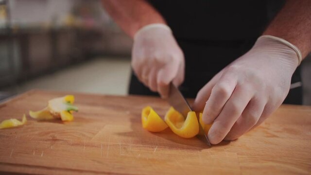 chef cook hand in medical gloves chopping yellow pepper for fresh greek salad