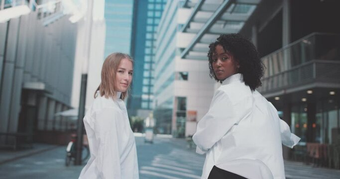 A ethiopian and caucasian young women looking to the camera in the businees area of a city