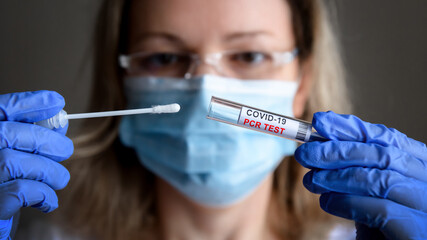 Coronavirus swab collection kit in doctor hands, tube to COVID-19 PCR testing close-up