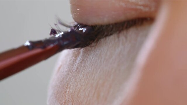 Face of a young girl in a modern eyelash lamination procedure in a professional beauty salon. Master apply black dye paint to the eyelashes during the eyelash curling procedure with a special brush.