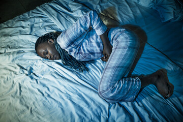 dramatic home portrait of young sick and depressed black African American girl sitting on bed ...