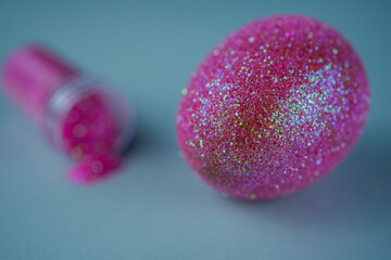Trendy Easter background with shiny pink colored egg on a blue light background with empty bottle of glitter powder. Easter concept. Creative spring holiday image with painted chicken egg