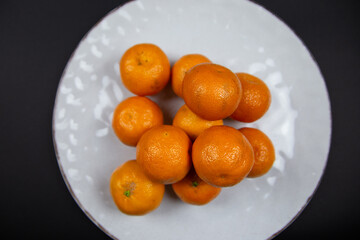 Large textured plate with tangerines, on a black background. Top view of fruits.