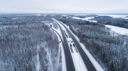 Beautiful road through the forest. Winter natural landscape. Cloudy snowy day.  Bird's eye. Travel concept