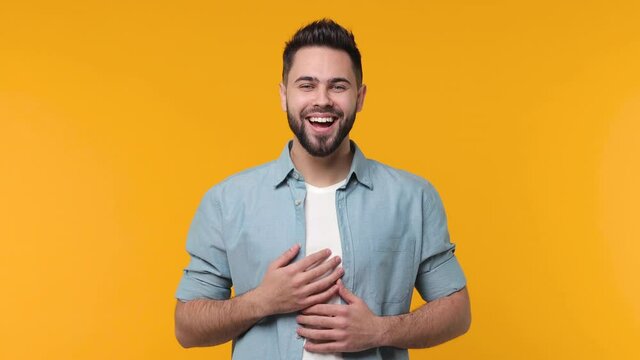 Surprised excited bearded young man 20s in casual blue shirt white t-shirt isolated on yellow background in studio. People sincere emotions lifestyle concept. Say wow covering mouth put hands on head