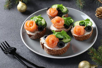 Sandwiches with salmon, cucumber, cream cheese and black olives on gray background. Homemade holiday snack. Closeup