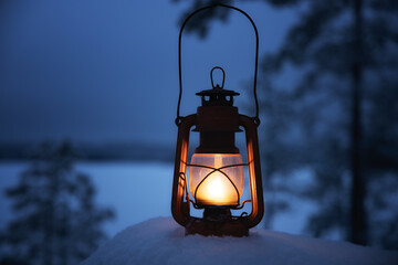 Vintage lantern outside with a snowy winter scene in background. Beautiful winter landscape with snow covered trees.
