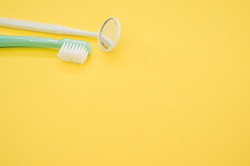 New green toothbrush and a yellow dental mirror on a yellow background
