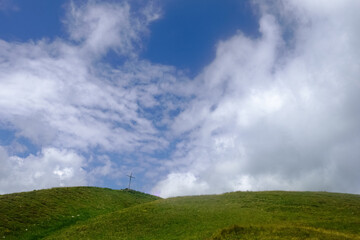 green hills with a summit cross and white clouds