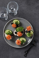 Sandwiches with salmon, cucumber, cream cheese and black olives on gray background. Homemade holiday snack. Top view