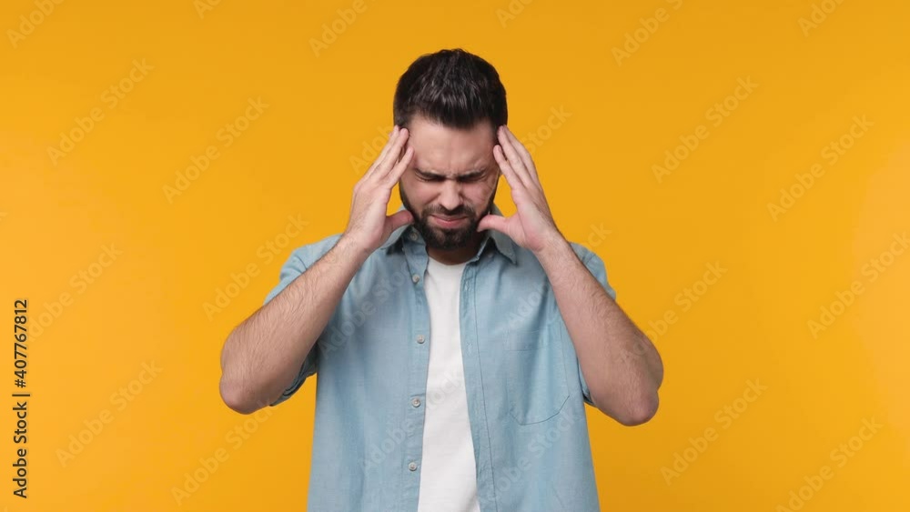 Wall mural Sick ill bearded young man 20s years old in blue shirt isolated on yellow color background in studio. People lifestyle concept. Put hands on head rub temples having headache migraine feel bad seedy