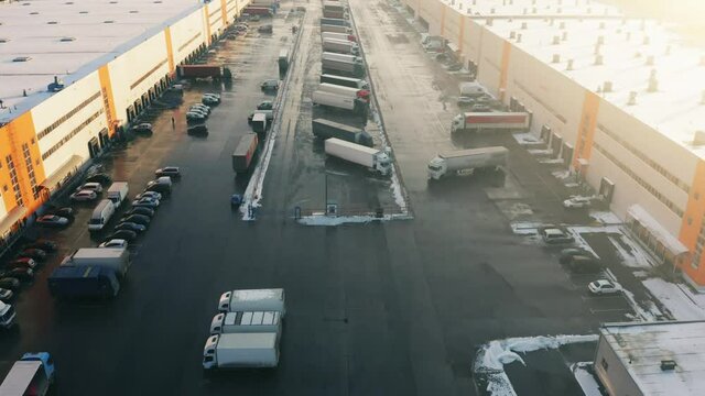 Logistics park with a loading hub. A lot of semi-trailer trucks stand at the warehouse ramps for load and unload goods from cargo containers. Aerial view