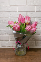 Bouquet of beautiful pink spring tulips in glass vase on wooden table near white brick wall. Concept of international women's day, mother's day, easter. Copy space. Valentine love day