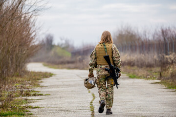 Beautiful girl in military uniform with an airsoft gun walking on the road