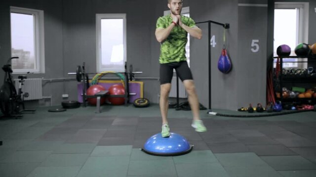 Athletic man in activewear doing side lunge exercised on Bosu doing functional workout in gym 