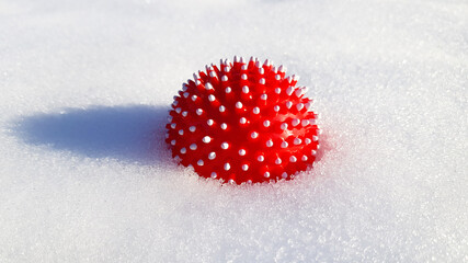 Obraz na płótnie Canvas Red ball with spikes in the form of a corona virus is half buried in the snow. Ball for dog or self massage. Place for text.
