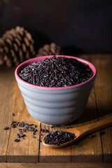 Black wild rice in ceramic bowl on wooden background. Thai black jasmine rice (Rice berry).