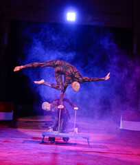 twins acrobats in neon costumes stand on their arms, ultraviolet makeup