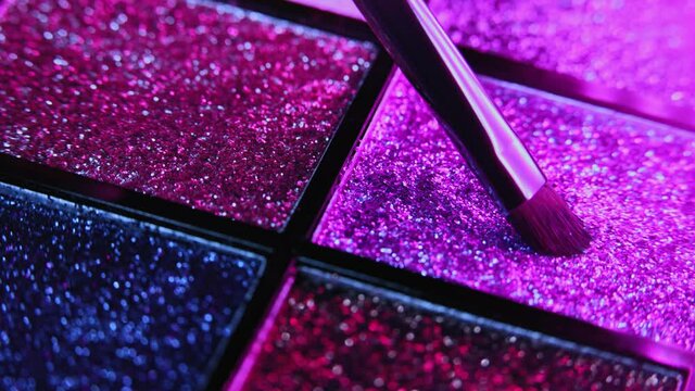 Brush gains eyeshadow glitter on pile to be used in make-up. Artist working with palette, variation of shiny textures. Details of working process, tools in beauty industry. Decorative cosmetics.