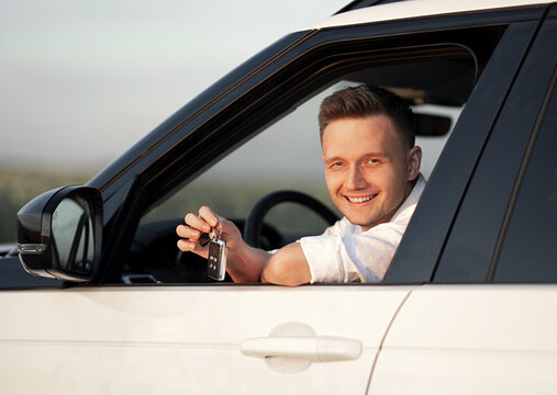 Successful happy young European man showing the keys sitting in the new white car. concept of buying or renting a car. Close up portrait photo 