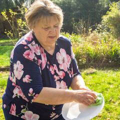 Plump mature woman washes dishes in her garden