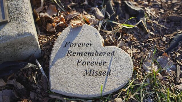 Slow Motion Close Up of Heart Shaped Grave Stone Saying Forever Remembered Forever Missed in Stone and Text on Grass and Ground