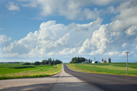 Rural highway in southern Minnesota with fields and a farm beneath dramatic clouds