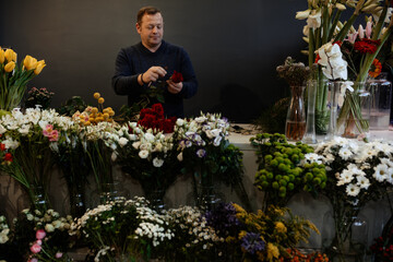 Happy caucasian florist making bouquets of red and pink roses for valentine's day. Concept of human emotions, facial expression, love, and hard work in this pandemic times.