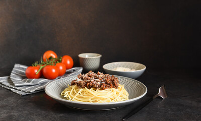 Spaghetti with bolognese sauce, basil and parmesan on a dark concrete background.