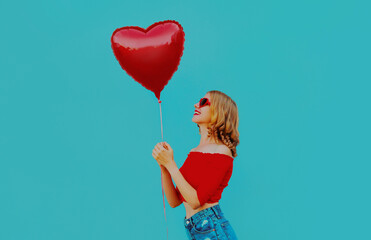 Portrait of cute smiling woman with red heart shaped balloon on a blue background